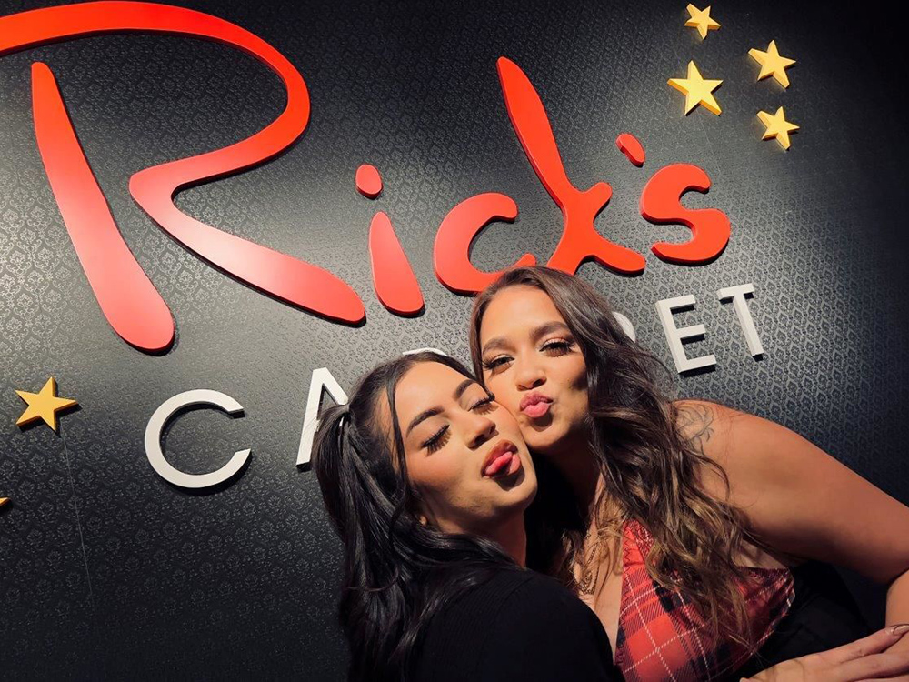 Two sexy girls making silly faces infront of Ricks Sign